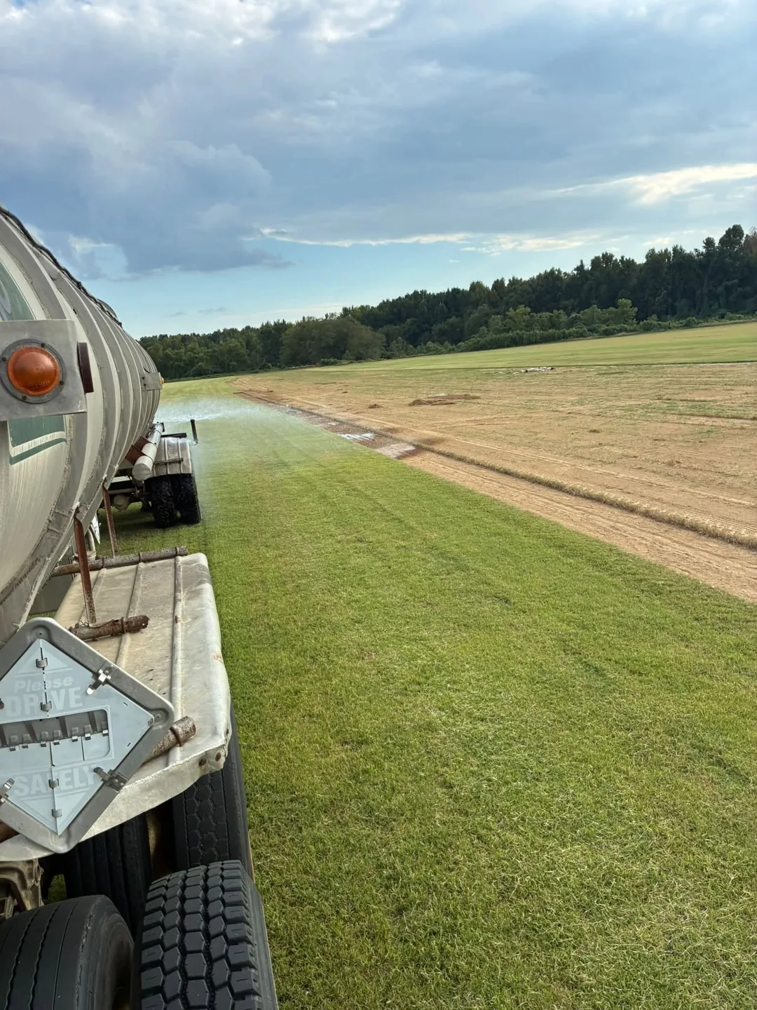 Sod field and dirt track viewed beside a farm vehicle